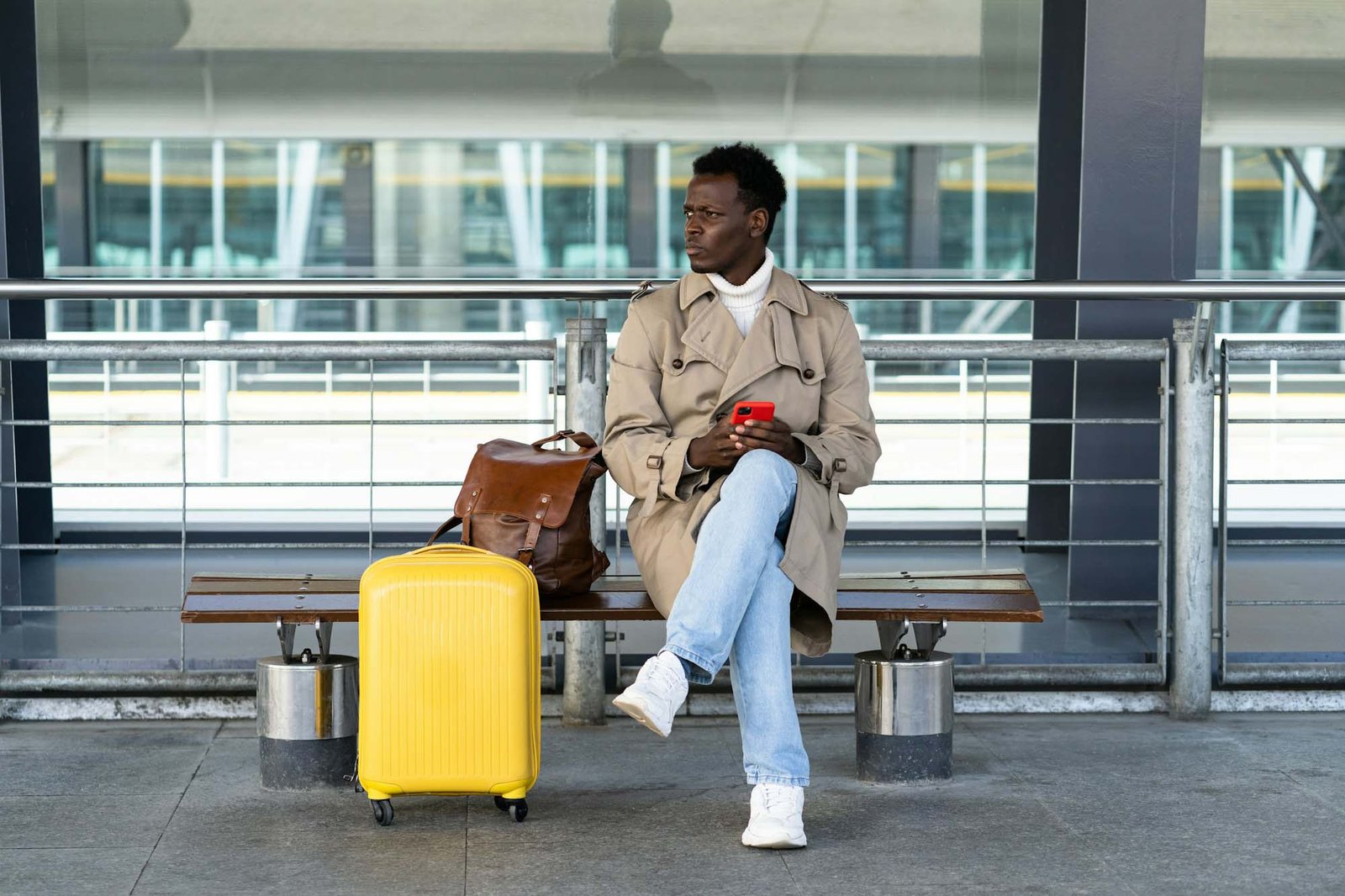 Homme voyageur assis sur un banc à l’aéroport, utilisant son téléphone pour appeler un taxi